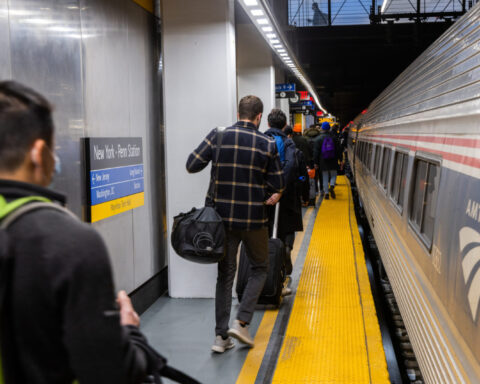 Interior photo of train station, people walking away down platform alongside waiting train.