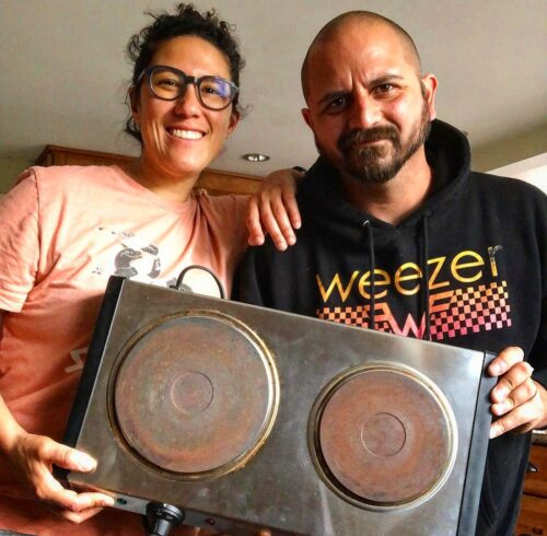 A woman and a man pose for a close-up photo holding an electric hot plate.