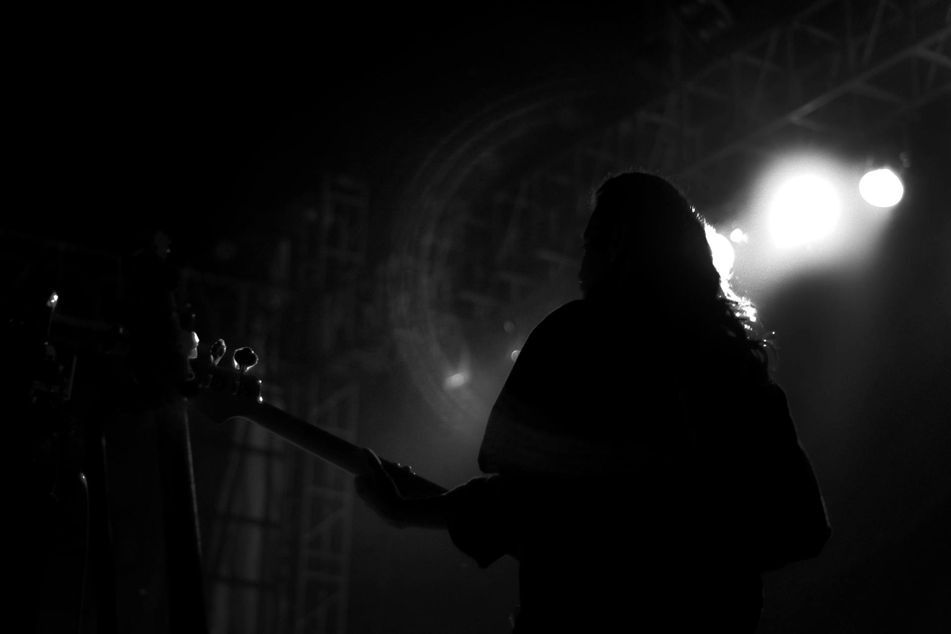 Silhouetted guitarist performing under stage lights during an intimate live music set