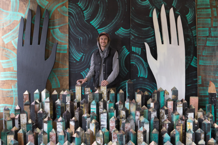 Artist Wes Bruce stands among sculptural installation elements as part of his immersive community-centered artistic practice.