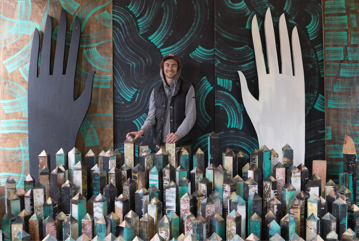 Artist Wes Bruce stands among sculptural installation elements as part of his immersive community-centered artistic practice.
