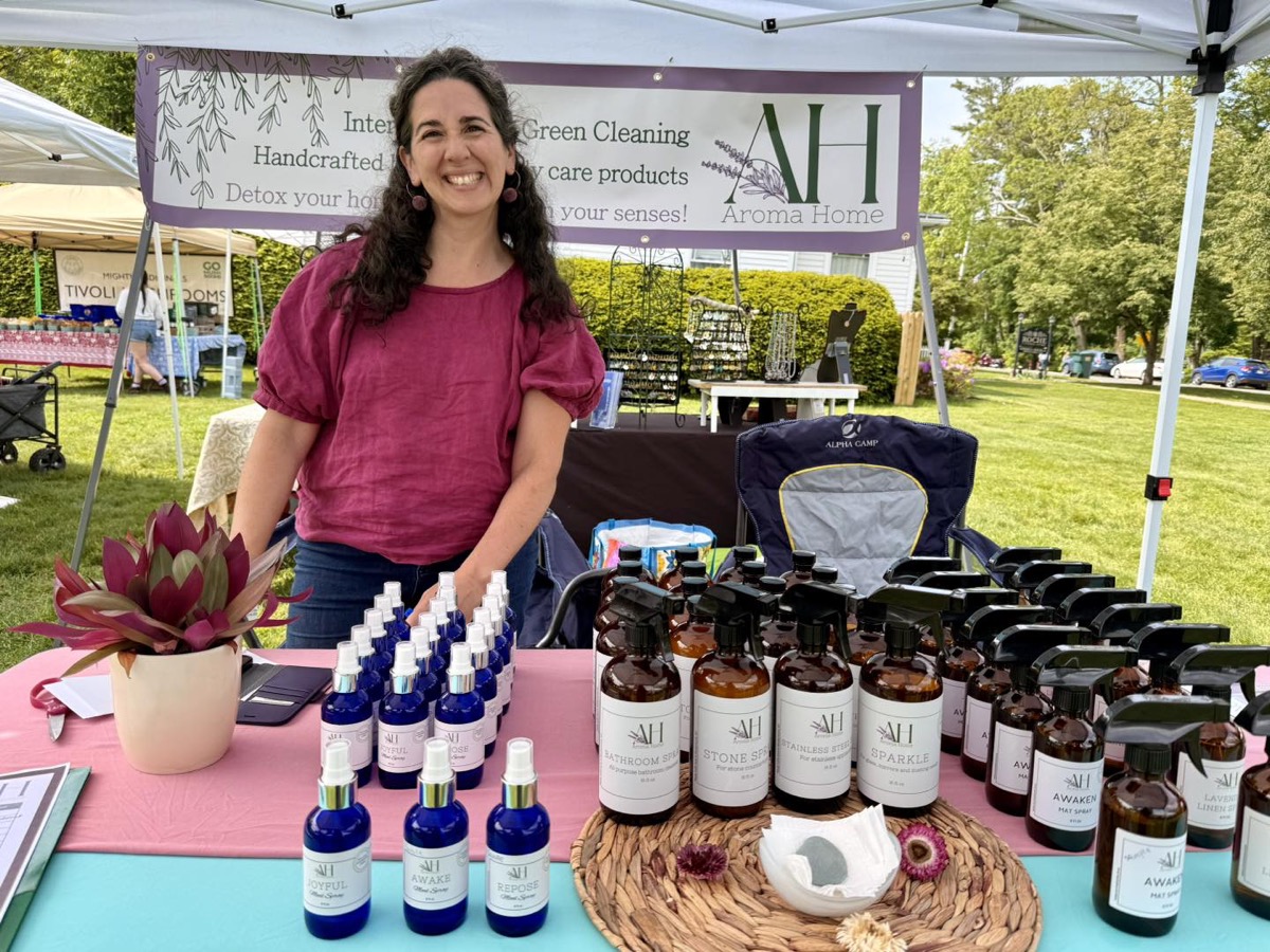 Monika of Aroma Home at a Lenox market event, with handmade home and body care products displayed under a vendor tent.